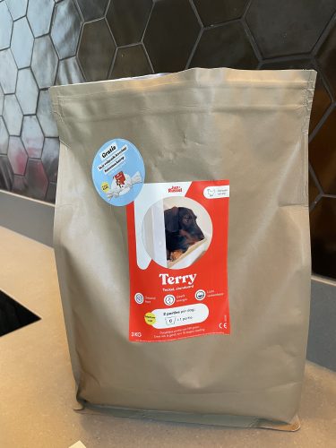 Verpakking van hondenvoer voor teckels met de naam 'Terry' en een afbeelding van een teckel op de voorkant, geplaatst op een moderne keukentafel.